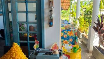 Una habitación con una puerta azul, una máquina de escribir, un barril amarillo y una mesa con mantel floral.