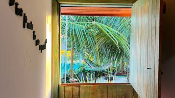 A room with a bed, a window with a view of palm trees, and a wooden ceiling.