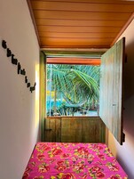 Quarto com cama, janela vista para palmeiras e teto de madeira.