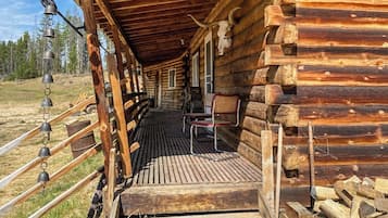 A wooden cabin with a porch, a bench, and a set of hanging bells.