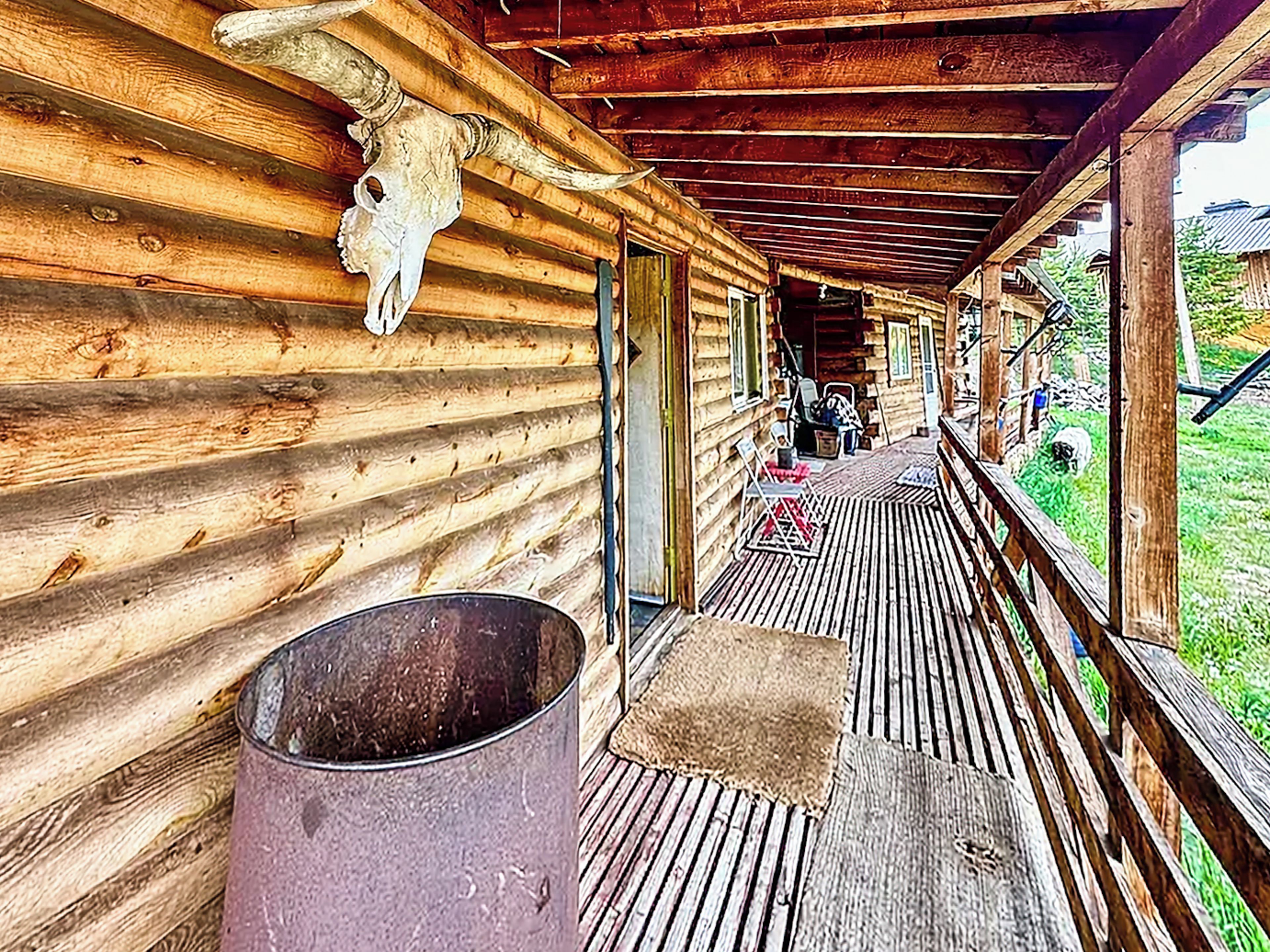 En træhytte med veranda, en metalspand og et oksehoved monteret på væggen.