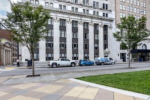 A building with large columns and a flat facade, parked vehicles, and a sidewalk with trees.
