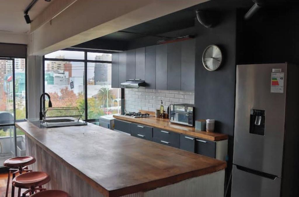 A modern kitchen with a large island, stainless steel appliances, and a view through the window.