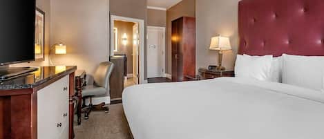 Une chambre d’hôtel avec un grand lit, un bureau doté d’un téléviseur à écran plat, une chaise, une table de chevet avec une lampe et une porte donnant sur une autre pièce.