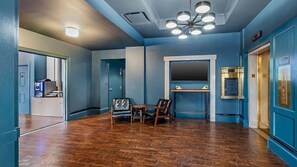 Un hall d’hôtel avec un plancher en bois, un coin salon avec deux fauteuils, une petite table et un téléviseur fixé au mur.