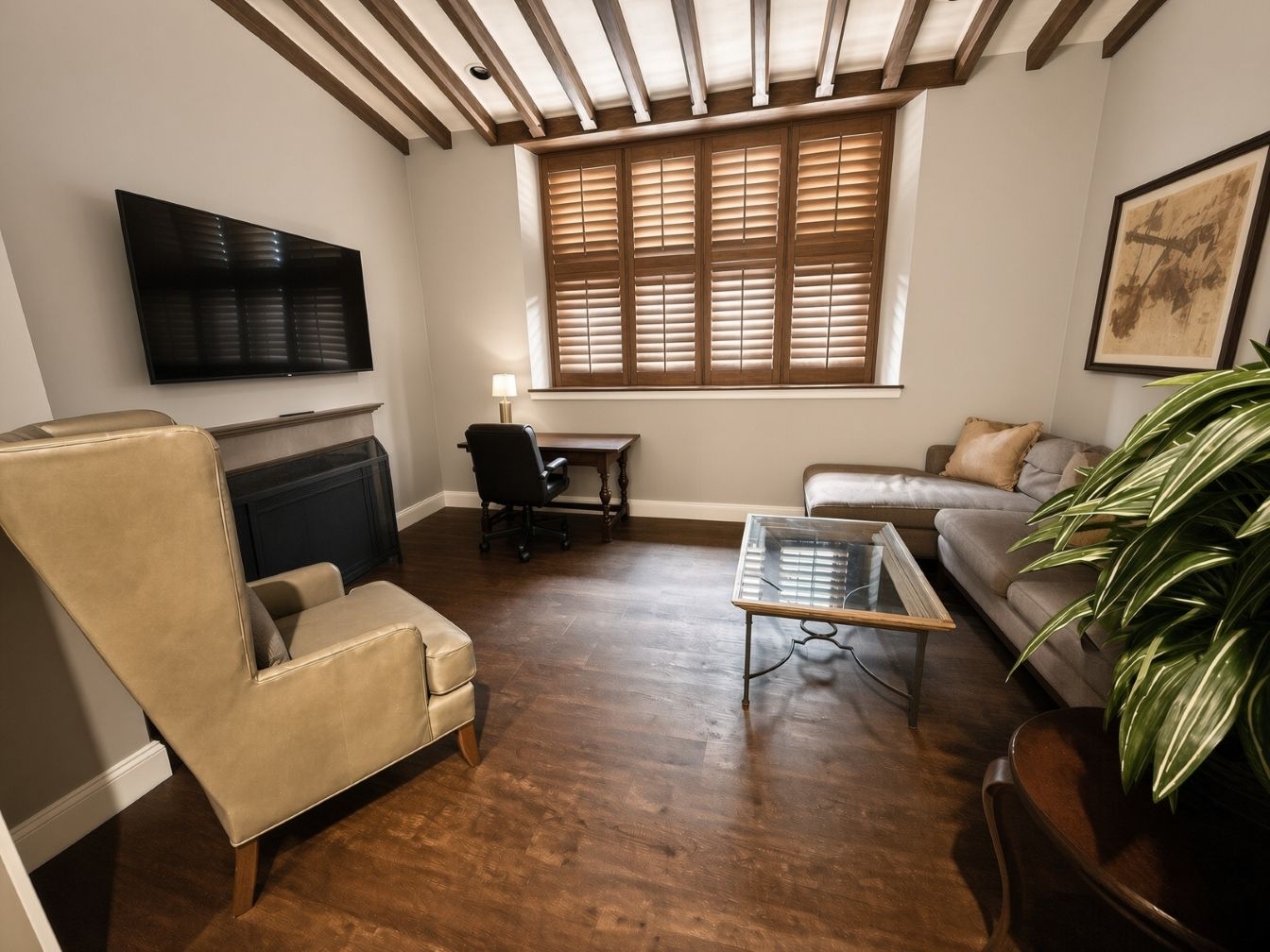 Una sala de estar con un sillón de cuero, una mesa de centro de vidrio, un sofá, una chimenea, un televisor y un ventanal grande con persianas.
