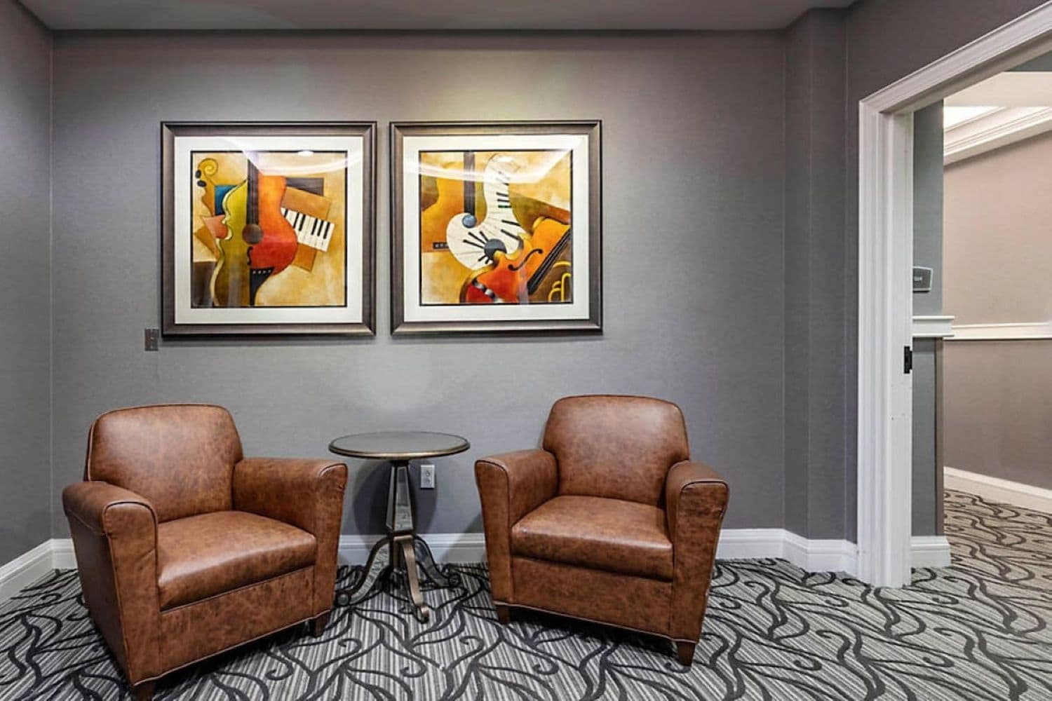 Une pièce comprenant deux fauteuils en cuir, une petite table ronde et deux tableaux abstraits encadrés accrochés au mur.