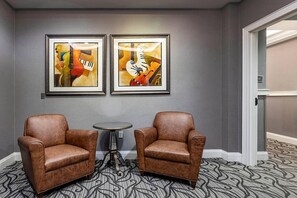 Une pièce comprenant deux fauteuils en cuir, une petite table ronde et deux tableaux abstraits encadrés accrochés au mur.
