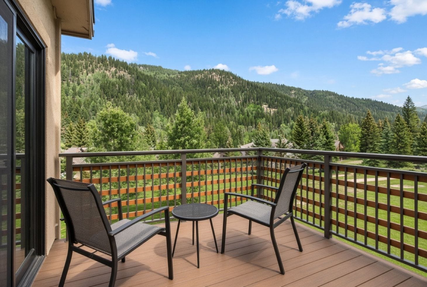 A balcony with two chairs and a table, overlooking a forested mountain.