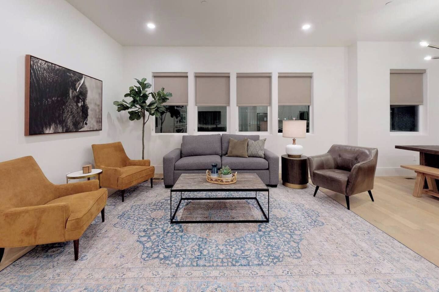 A modern living room with a grey sofa, two armchairs, a coffee table, and a large plant.