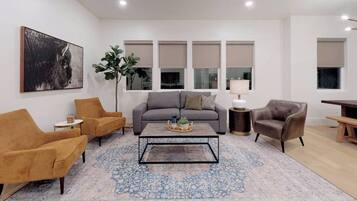 A modern living room with a grey sofa, two armchairs, a coffee table, and a large plant.