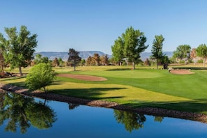 Un campo da golf con uno stagno che riflette gli alberi e un cielo sereno.