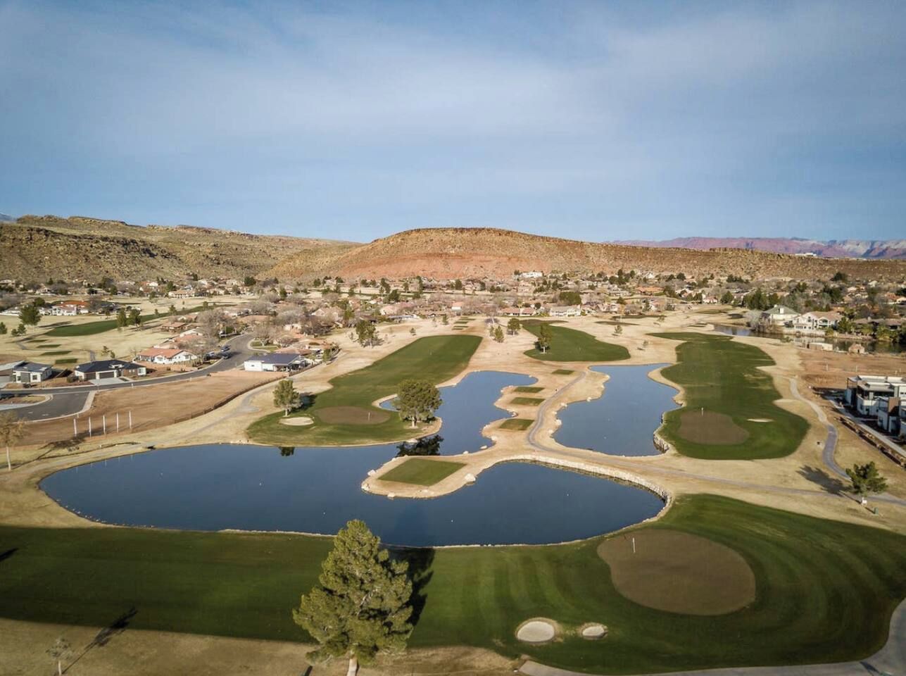 An aerial view of a golf course with multiple ponds and a residential area in the background.