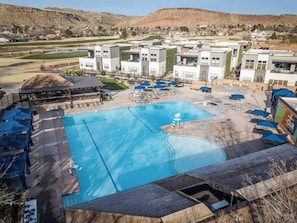 Ein Schwimmbecken mit Liegestühlen und Sonnenschirmen, umgeben von modernen Gebäuden mit Blick auf eine hügelige Landschaft.
