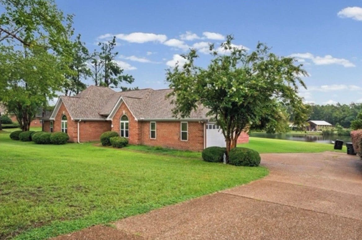 A brick building with a sloped roof, a paved driveway, and a well-maintained lawn.