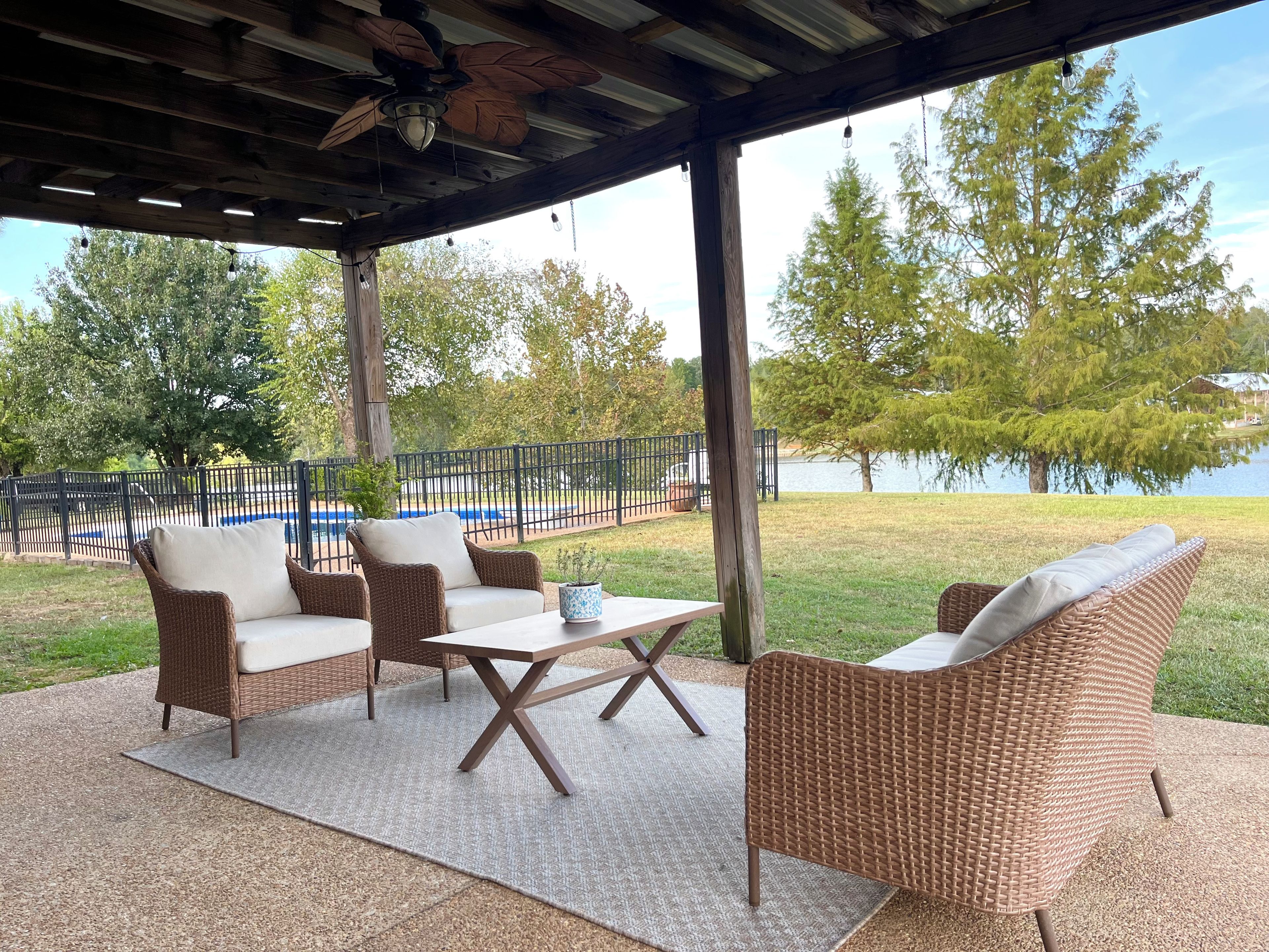 Un patio exterior con mobiliario de mimbre, una mesa y vistas a un lago.