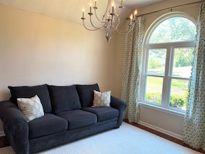 A dark-colored sofa with patterned cushions, a white rug, and a chandelier. - Cedar Lake Cottage • Pool & Lake view! (Oxford)