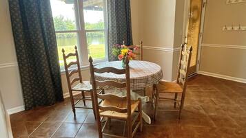 Un coin repas avec une table ronde, des chaises, un lustre et une vue par la fenêtre.