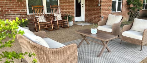 Un patio techado con mobiliario de mimbre, una mesa de madera y una planta en maceta.