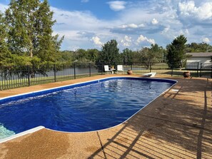 A swimming pool with a black metal fence, surrounded by trees and a clear sky.