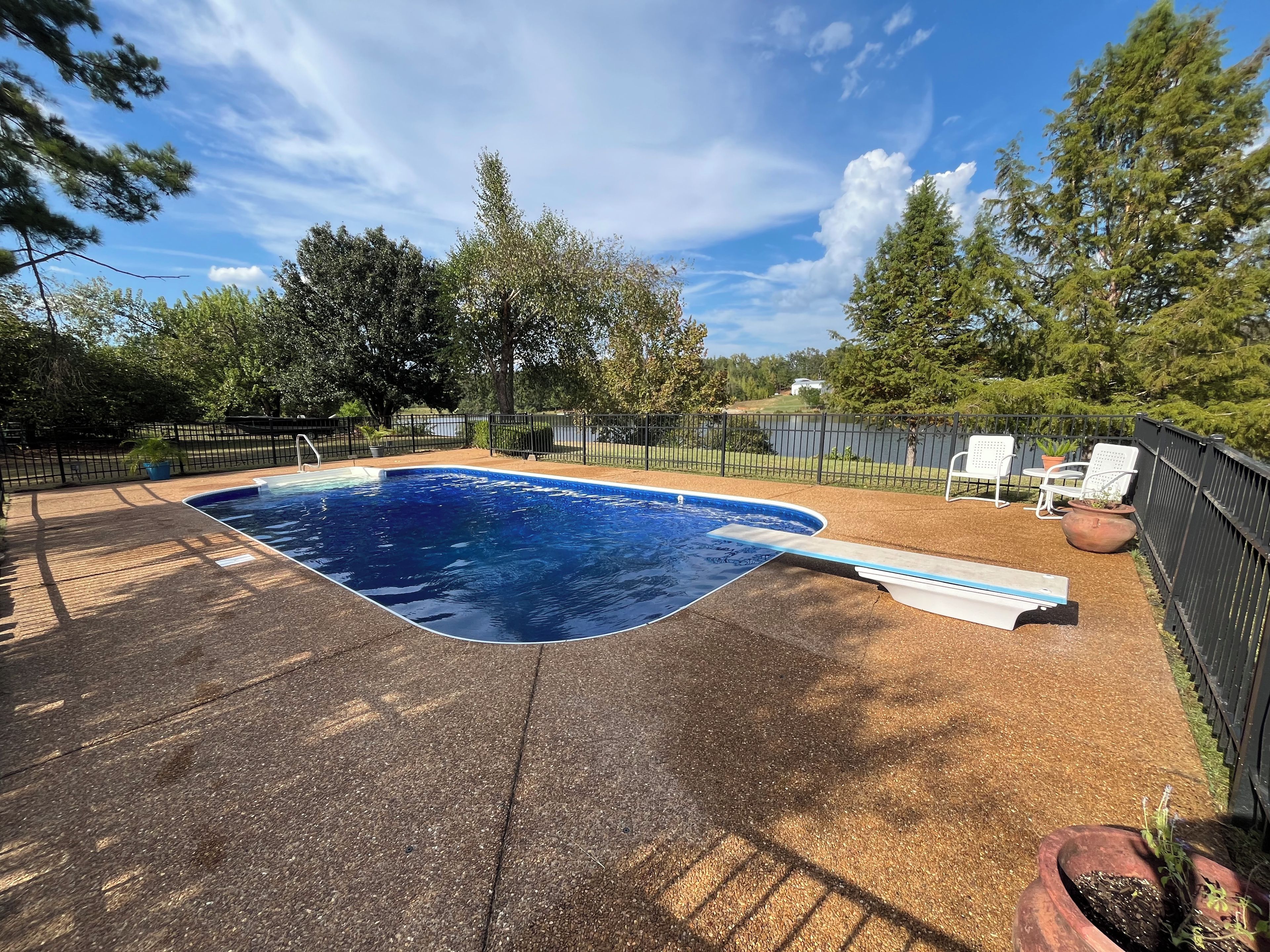 A swimming pool with a deck, surrounded by a fence and trees.