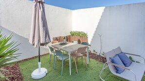 Une terrasse avec une table et des chaises, un parasol et un petit jardin agrémenté de plantes.