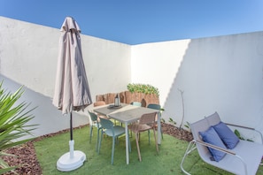 Un patio con una mesa y sillas, una sombrilla y un pequeño jardín con plantas.