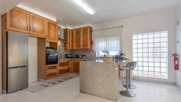 A modern kitchen with wooden cabinets, a stainless steel refrigerator, a built-in oven, and a granite countertop island with bar stools.