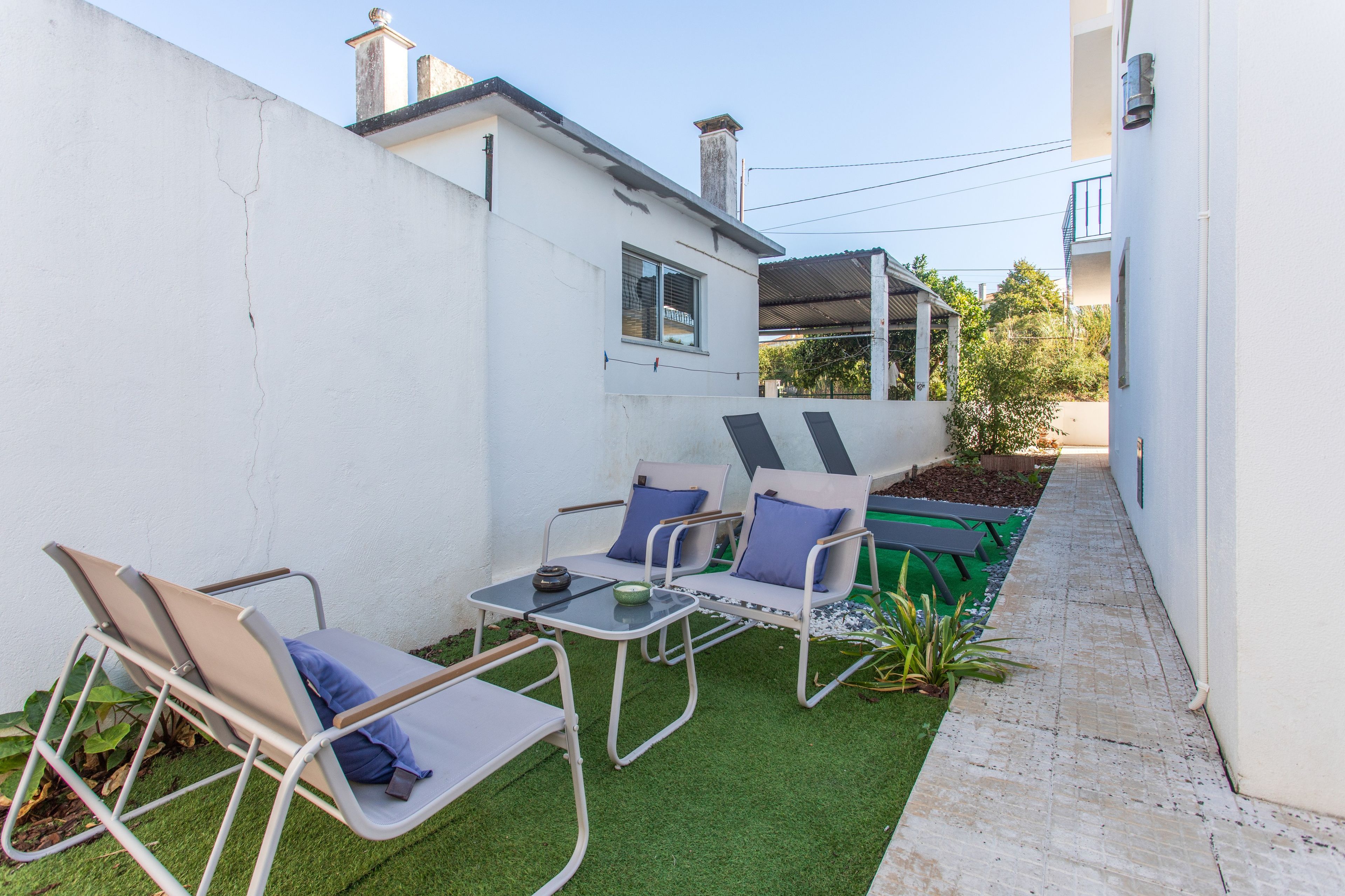 Un patio con dos sillones de descanso y una mesa pequeña, rodeado por un muro blanco y una zona de césped artificial verde.