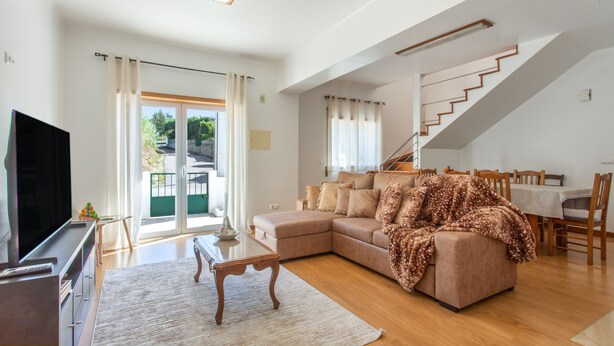 Un salon spacieux avec un grand canapé, un téléviseur à écran plat et un escalier menant à l’étage supérieur.
