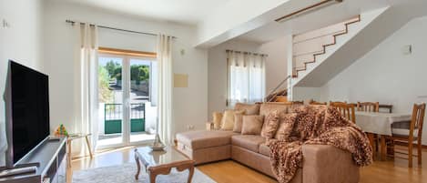 A spacious living room with a large sofa, a flat-screen TV, and a staircase leading to an upper level.