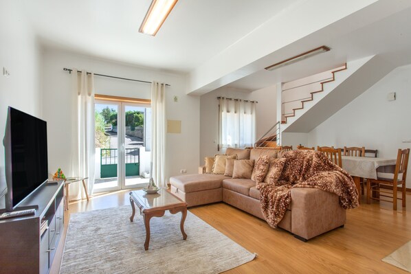 A spacious living room with a large sofa, a flat-screen TV, and a staircase leading to an upper level.