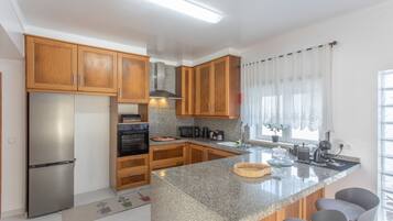 Een moderne keuken met houten kastjes, een roestvrijstalen koelkast, een inbouwoven en een granieten aanrecht.