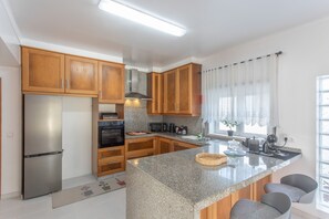 Cozinha moderna com armários de madeira, geladeira de aço inoxidável, forno embutido e bancada de granito.