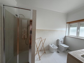 Un baño moderno con cabina de ducha de vidrio, un bidé, un inodoro y una ventana con persianas.