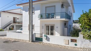 Un immeuble résidentiel de deux étages doté d’un balcon, d’un escalier et d’une voiture garée devant.