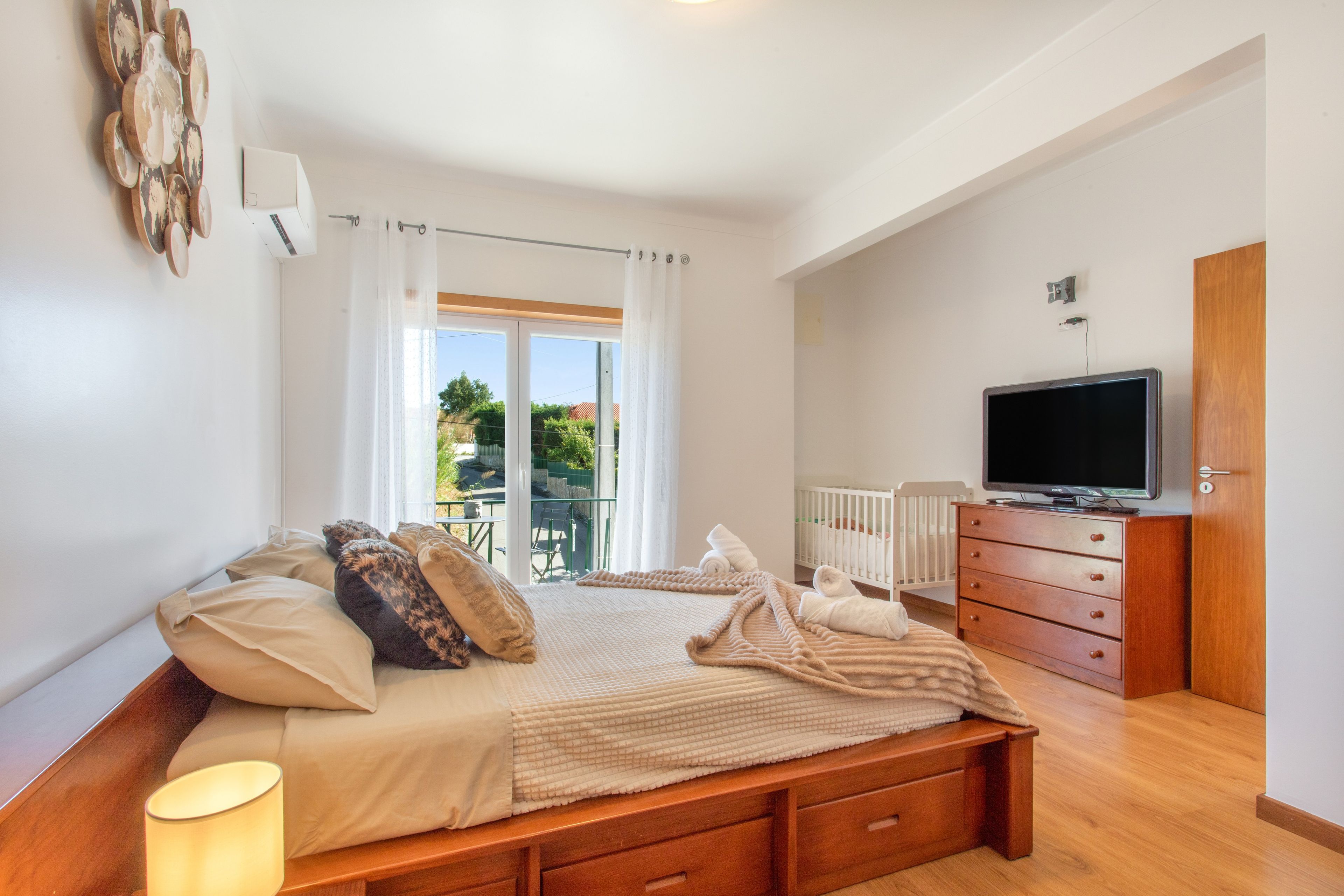 Un dormitorio con cama, televisión, cómoda y vistas al exterior.