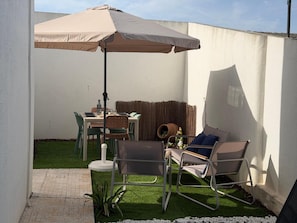 Un patio con mesa y sillas, una sombrilla grande y un pequeño jardín.