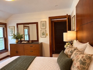 Ein Schlafzimmer mit einem Bett, einem Schminktisch, einem Spiegel und einer Tür zu einem weiteren Raum.