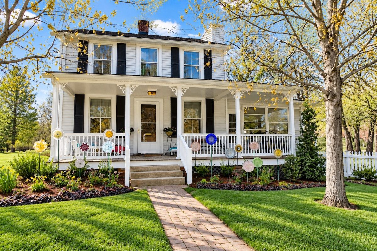 A two-story house with a front porch, a pathway leading to the entrance, and a tree in the foreground.