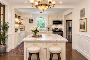 A spacious kitchen with a marble island, stainless steel appliances, and a decorative chandelier.
