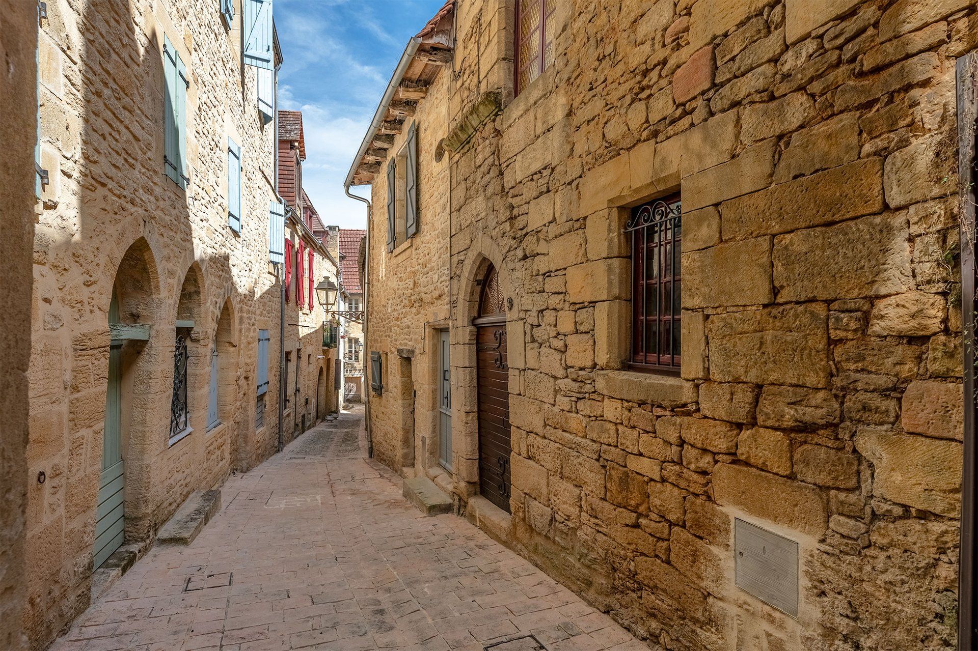 Eine enge, mit Kopfsteinpflaster belegte Straße, gesäumt von historischen Gebäuden mit Rundbogenportalen und traditionellen Fensterläden.