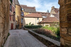 A narrow cobblestone street flanked by historic stone buildings with red-tiled roofs and traditional shutters. - Hostcare - Le Petit Château – Downtown (Sarlat-la-Canéda)