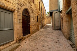 A narrow cobblestone alleyway between stone buildings with arched doorways and a grey door on the left. - Hostcare - Le Petit Château – Downtown (Sarlat-la-Canéda)