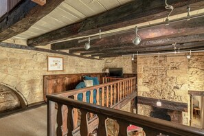 A rustic interior with a stone wall, wooden beams, a wooden bench, and a television. - Hostcare - Le Petit Château – Downtown (Sarlat-la-Canéda)
