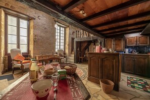 A rustic kitchen with wooden cabinets, a dining area with a table set for two, and a stone wall. - Hostcare - Le Petit Château – Downtown (Sarlat-la-Canéda)