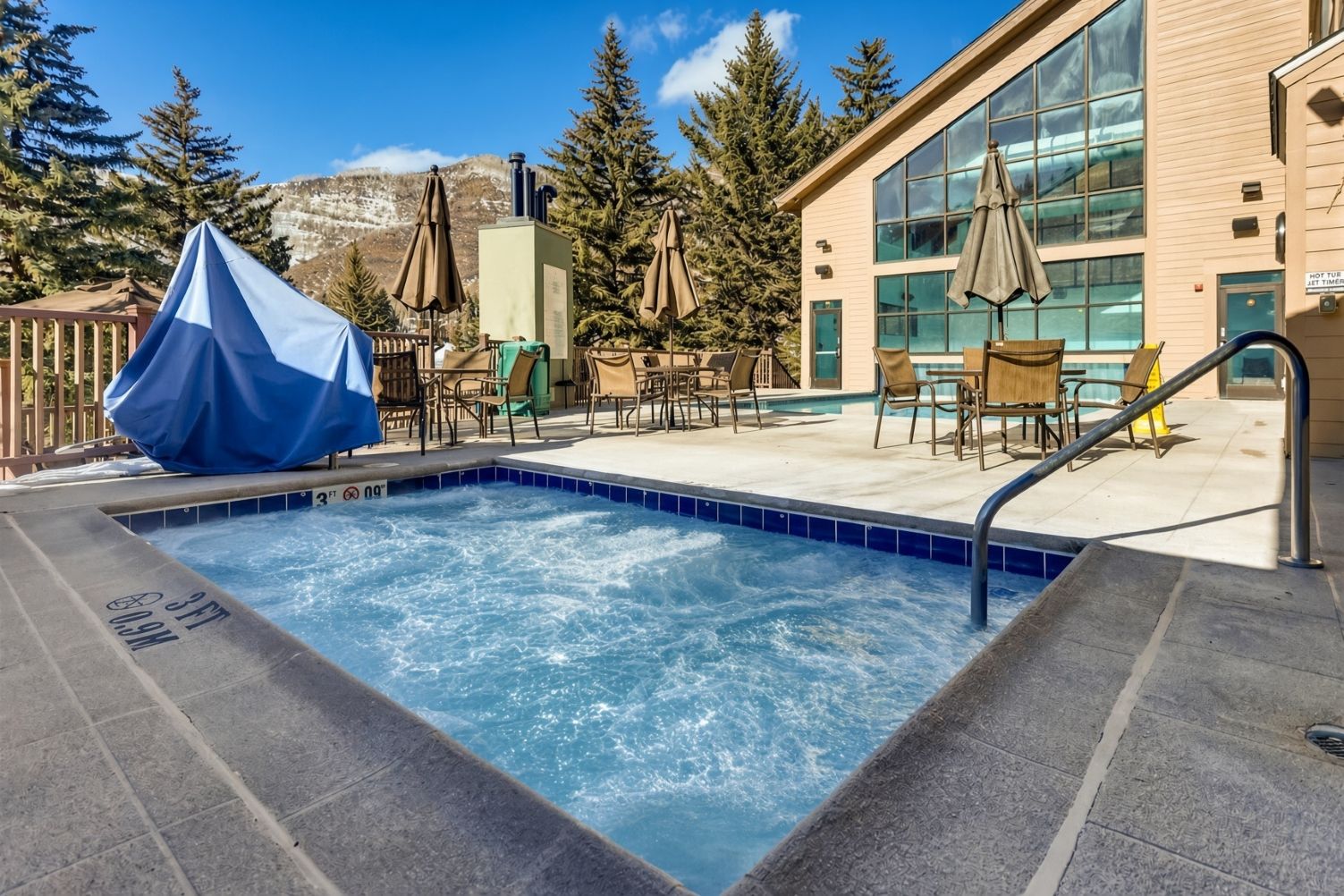 A pool area with a hot tub, lounge chairs, and umbrellas.