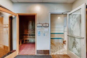 Un pasillo que conduce a una sauna y un baño de vapor, con suelo de baldosas y un banco de madera.