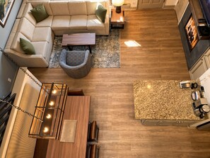 Una cocina moderna con encimera de madera, un comedor con mesa y sillas, un sofá con cojines y una lámpara colgante.