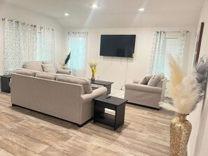 A modern living room with a sofa, two side tables, a flat-screen TV, and decorative plants. - 5BR All One Level | Fenced Yard | Pet Friendly (Richmond)